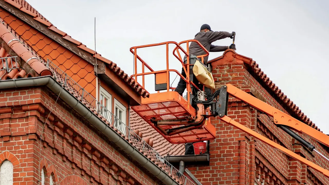 Operative in a raised platform repairing brickwork at the top of a chimney stack